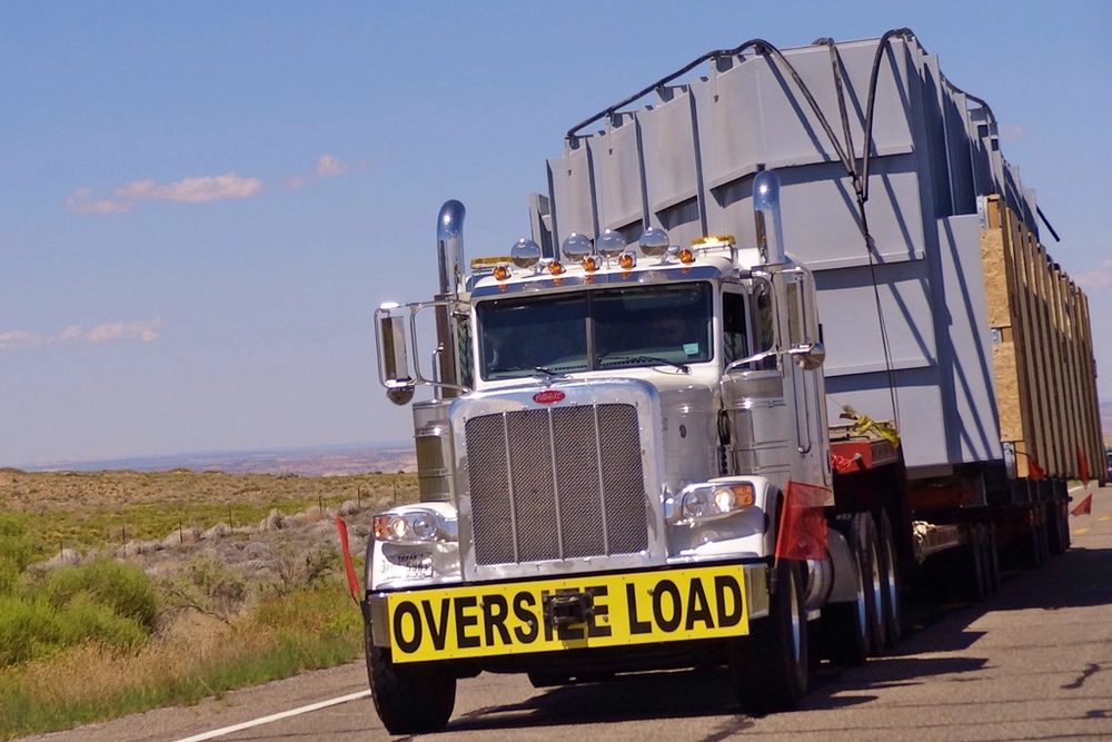 A tractor unit hauling an oversize load on a flatbed trailer along a highway