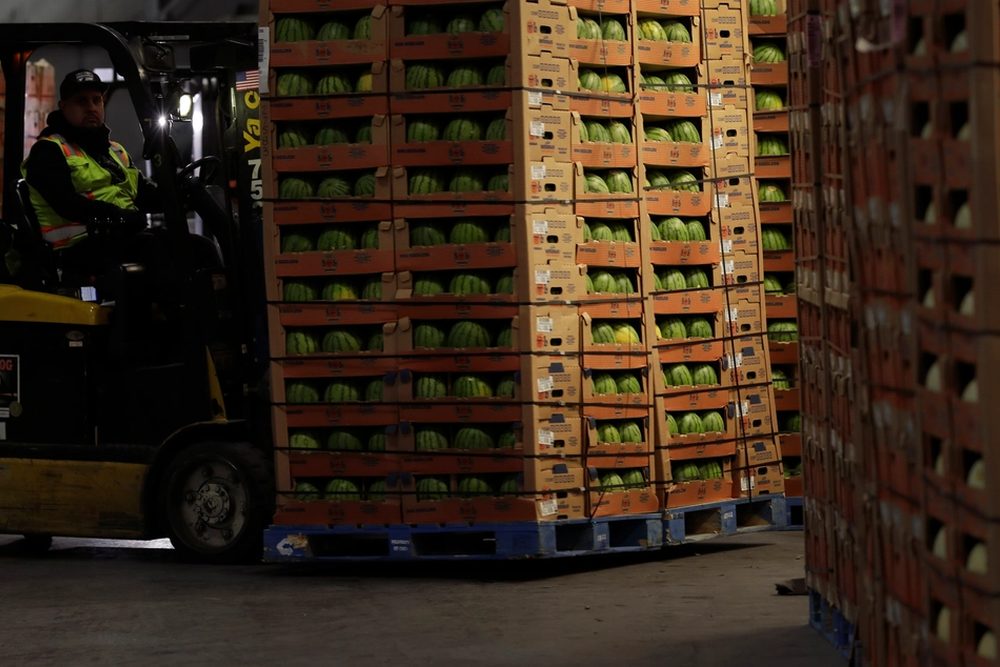 A forklift loading crates of melons onto a pallet inside a packing house
